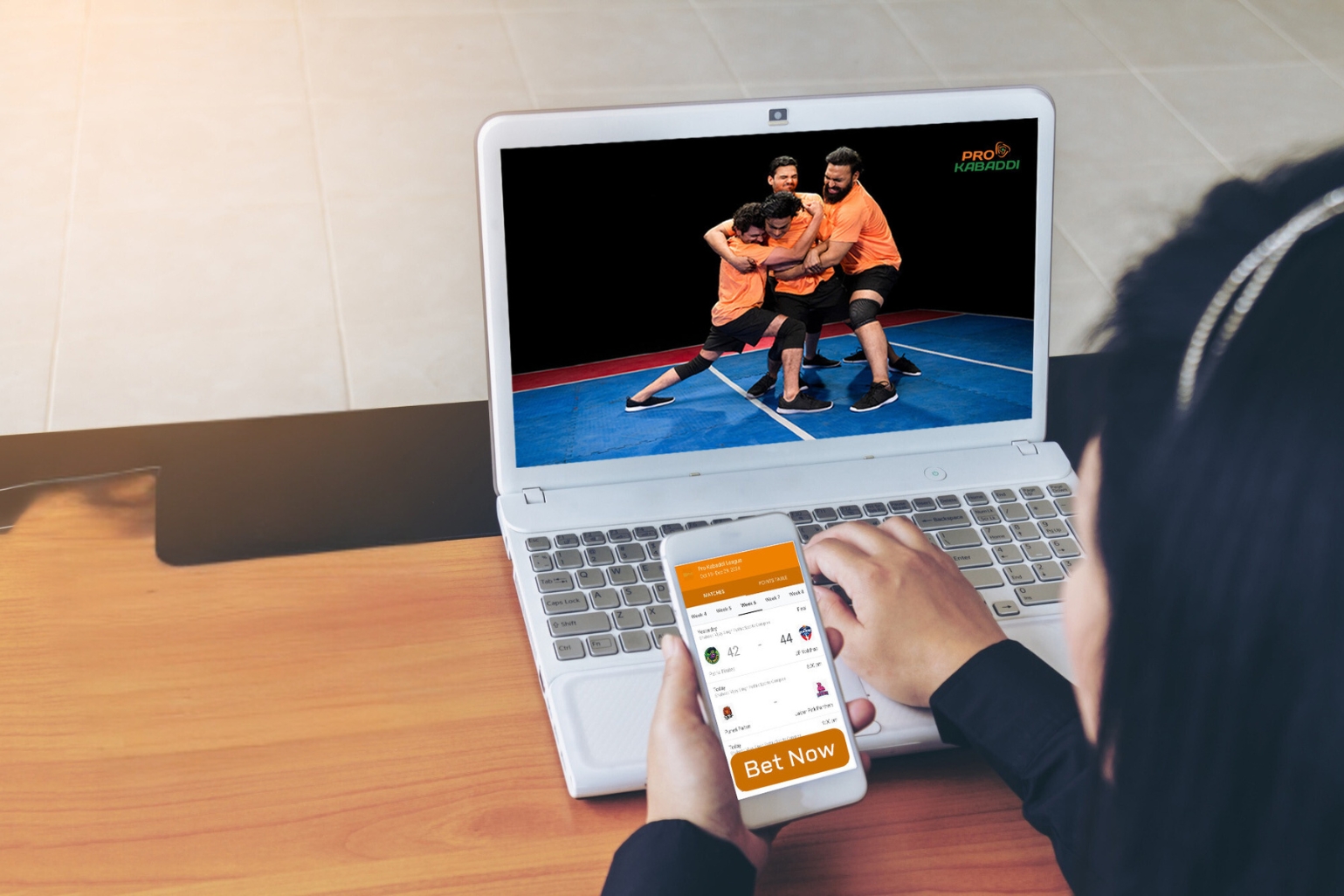 A woman is focused on a kabaddi video on her phone and laptop 